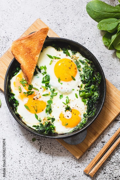 Obraz green shakshuka in a cast iron skillet. fried eggs with spinach and fried toast. healthy nutritious breakfast