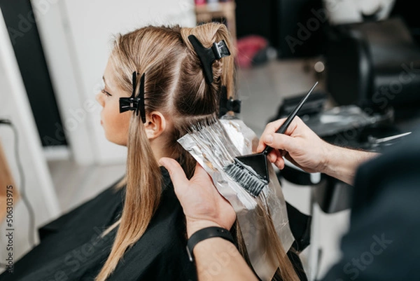 Fototapeta Hairdresser is applying bleaching powder on woman's hair and wrapping into the foil.