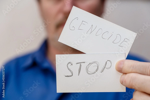 Fototapeta Stop War. The writing is in jagged gray letters on the paper. Man holds two white paper rectangles with handwritten text in front of his face. Close-up of a mature man's hand.