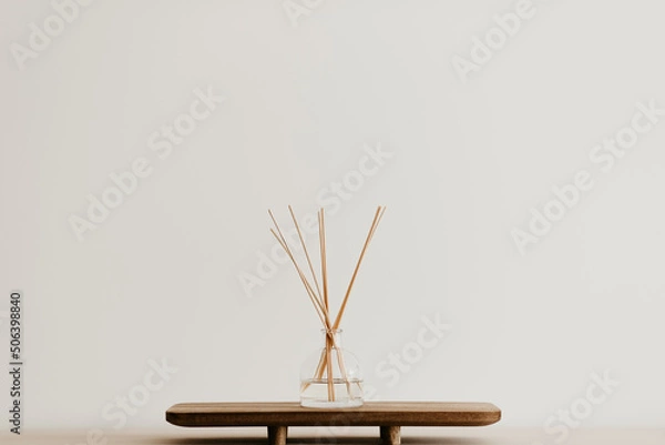 Obraz A glass reed diffuseron a wooden board. Simple home decoration idea. Nice scent, good fragrance. White wall background, copy space. Brown tones, minimal design. 