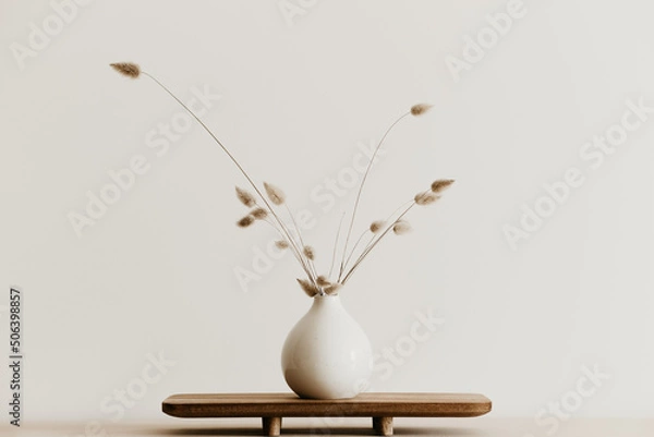 Obraz A bunch of  dried bunnytail flower in a white ceramic vase on a brown wooden board. Simple and minimal home decoration. White wall, copy space. 