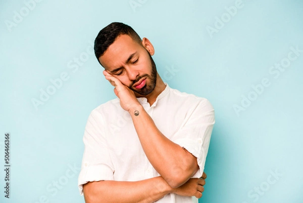 Fototapeta Young hispanic man isolated on blue background tired of a repetitive task.