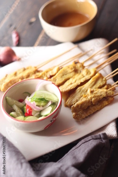 Fototapeta Pork satay served in a white plate with peanut and cucumber dipping sauce.