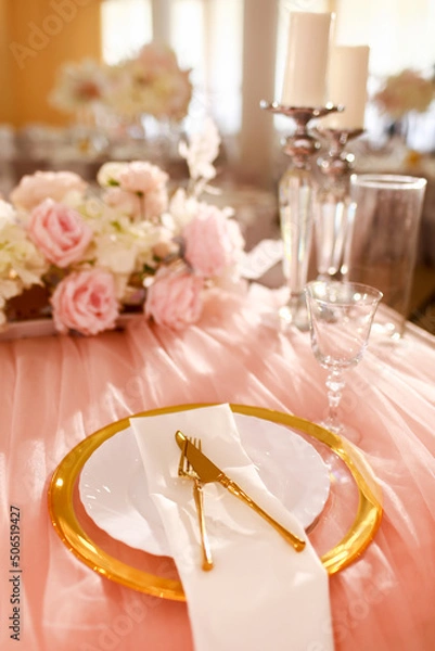 Obraz table decoration with pink tablecloth, crystal candlesticks with candles and white pink flowers in restaurant . stylish wedding day. setting table with gold plate, fork and knife