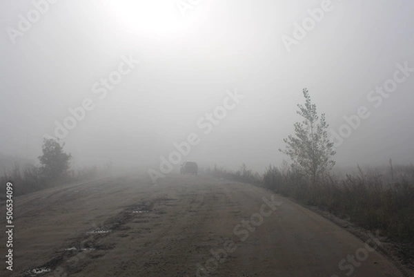 Fototapeta road travel with a car in heavy fog with precipitation in clouds