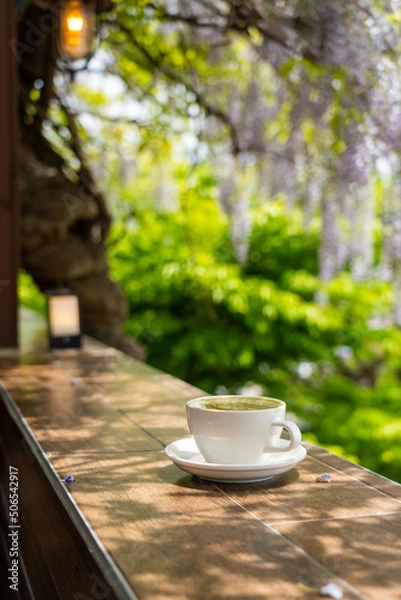 Obraz Hot cafe latte in a white ceramic cup tea set with purple wisteria flowers hanging at the garden in South Korea