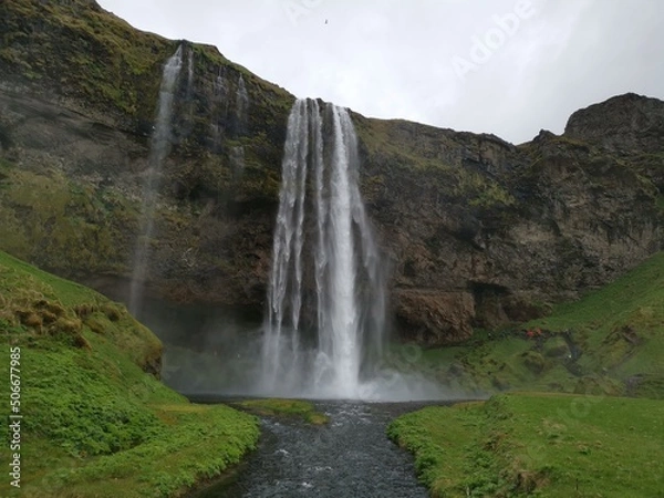 Fototapeta A foss waterfall in iceland with a grey sky and green grass around the river water flow on a roadtrip brak stop vacation