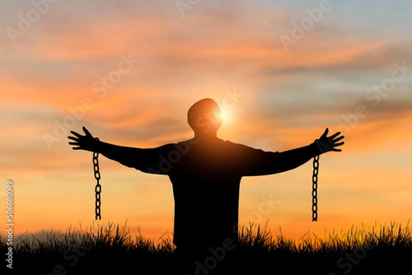 Fototapeta Silhouette of freedom young man standing alone with beautiful sky at sunset open both arms with chains on his arms. He felt free from the shackles tied to his arms.