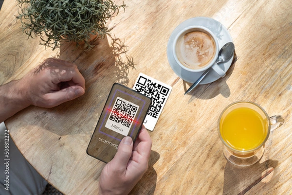 Fototapeta A customer scanning a qr code with his cell phone in a bar or restaurant to read the menu. The hospitality industry and new technologies
