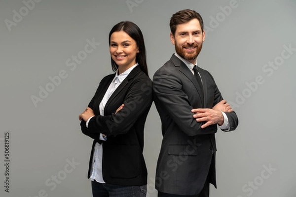 Fototapeta Concept of partnership in business. Young man and woman standing back-to-back with crossed hands against grey background