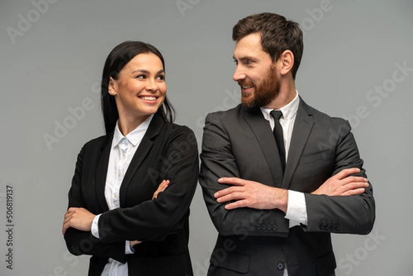 Fototapeta Confident happy young business partners looking at each other while posing isolated on grey background. Business concept