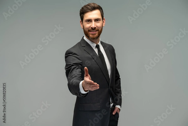 Fototapeta Male businessman in a suit stretching hand and shows a palm up gesture on a grey background. Concept of request, handshake