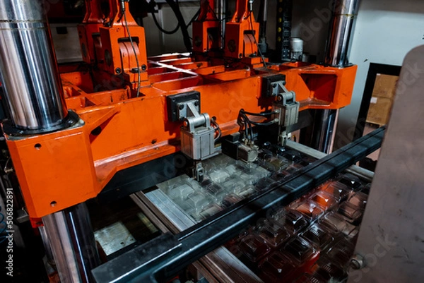 Fototapeta Vacuum thermoforming machine is used for producing plastic packaging in the factory. Close-up of the machine making a mold. Selective focus front