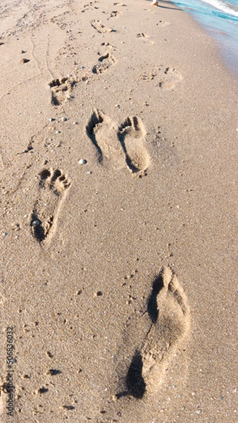 Obraz Footprints on the beach sand. Summertime sea. Footprints near the wave water. 