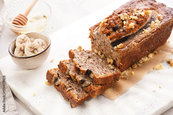 Fototapeta Chocolate banana bread with walnuts on a marble board and ingredients on a grey neutral background