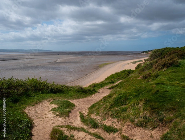 Fototapeta A clifftop view from the Wirral Country Park at Thurstaston looking down to the beach and across the Dee Estuary, at low tide, to the North Wales coast. Cloudy sky.