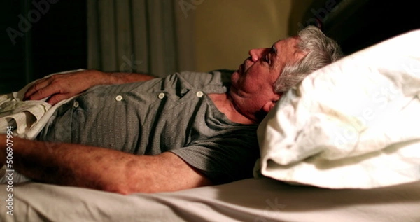 Fototapeta Old man in bed at night suffering from insomnia unable to sleep