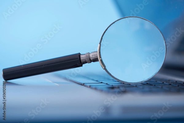Fototapeta magnifying glass resting on the laptop keyboard