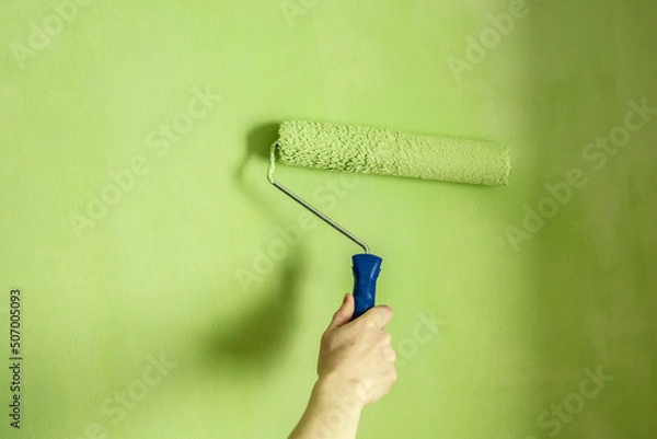 Obraz Hand is painting the wall green with a roller. Concept of renovation in the apartment. Closeup and copy space