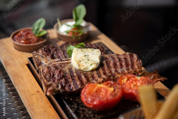 Obraz T-bone stek zaserwowany na gorącym kamieniu, z masełkiem czosnkowym oraz dodatkami