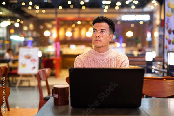Fototapeta Young man using laptop computer at coffee shop while thinking