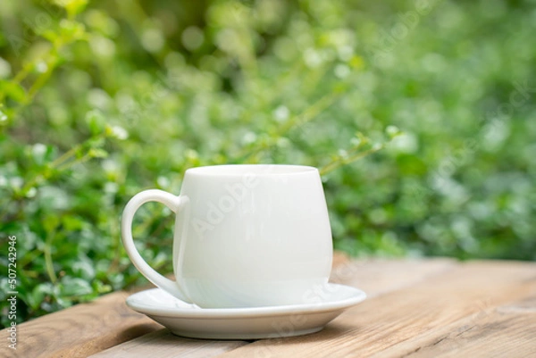 Fototapeta white ceramic coffee mug On the wooden floor, green tree bokeh background. soft focus.shallow focus effect.