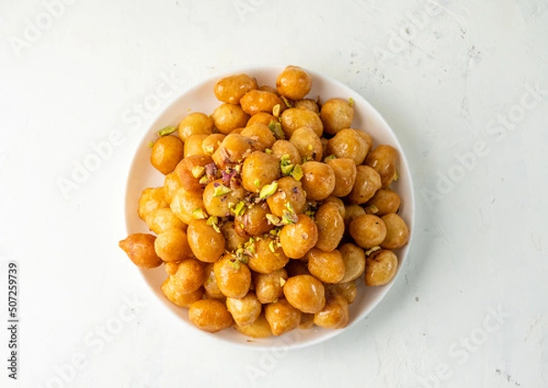 Obraz luqaimat or lokma in a sweet honey sauce in a white plate on a light background, top view, free space.