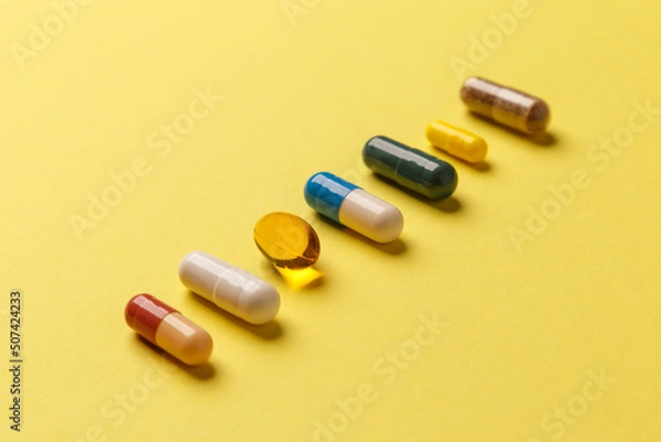 Fototapeta The concept of a healthy lifestyle. Various useful vitamin supplements on a yellow background. Medical pills of different colors. Close-up, side view. Medical preparations. Treatment of diseases.