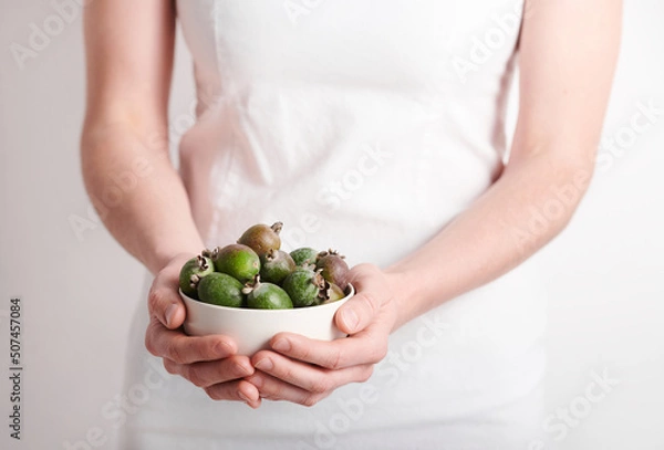 Fototapeta Horizontal medium section shot of unrecognizable woman wearing white clothes holding bowl full of pineapple guava fruits, copy space
