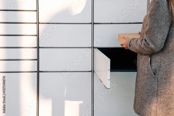 Fototapeta Post locker. Delivery automat terminal and hands with parcel courier box. Parcel delivery, pickup point with lockers, hand with parcel, contactless pack delivery.