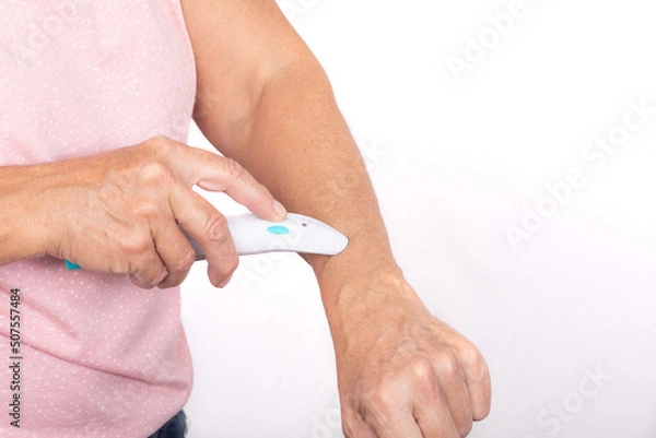Obraz A woman treats a mosquito bite on her arm with an electric bite healer - isolated on white background.