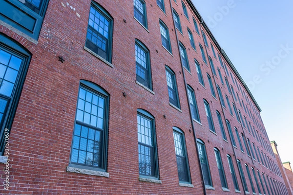 Obraz The fasade of a historic cotton factory building in an old industrial park on the Nashua River in May. Nashua, New Hampshire, USA
