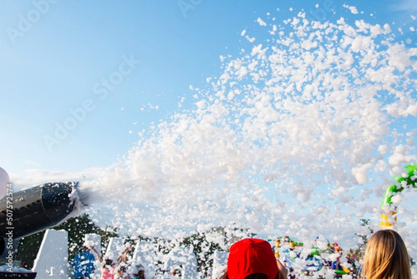 Fototapeta Foam party, foam cannon against the blue sky. girls admire the explosion of foam