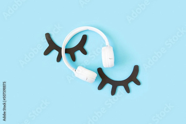 Obraz Eyelashes and white headphones on blue background. Concept Sleep learning, audiobook or lullaby for the night. Top view Flat lay