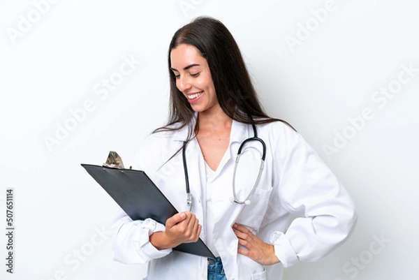 Fototapeta Young caucasian woman isolated on white background wearing a doctor gown and holding a folder
