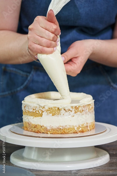 Fototapeta a woman's hand squeezes cream from a culinary bag onto a biscuit for a round-shaped cake. creating a birthday cake.