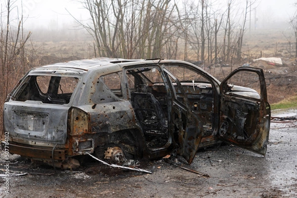 Fototapeta Burnt car during the war in Ukraine. Destroyed buildings, roads. Technique of civilian Ukraine.