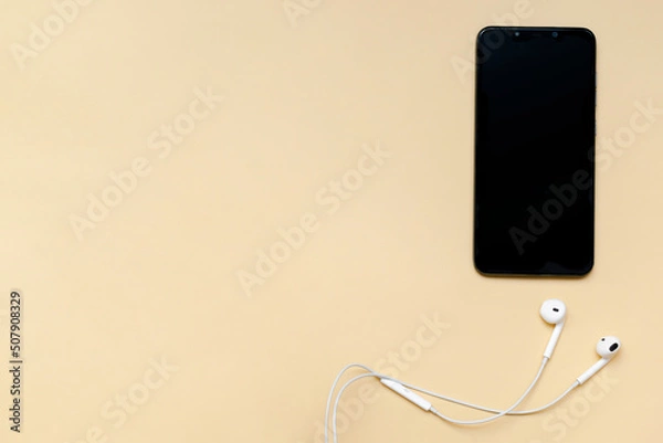 Fototapeta Top view of black smartphone with blank screen and wire headphones, mobile phone as music gadgets on beige background top view copy space