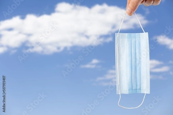 Fototapeta Coronavirus goodbye concept. Hand Raised Up a Medical Mask into the Sky.