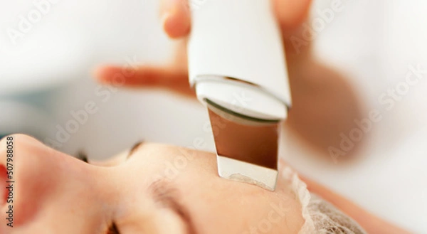 Obraz Beautician cosmetologist doing ultrasonic facial cleansing skin with device, professional cosmetic procedure in a beauty clinic salon for client. Skincare and machine cosmetology spa concept.	
