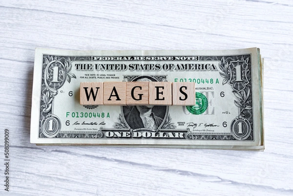 Fototapeta Wages word written on wood block with American Dollar-bills. Directly above.