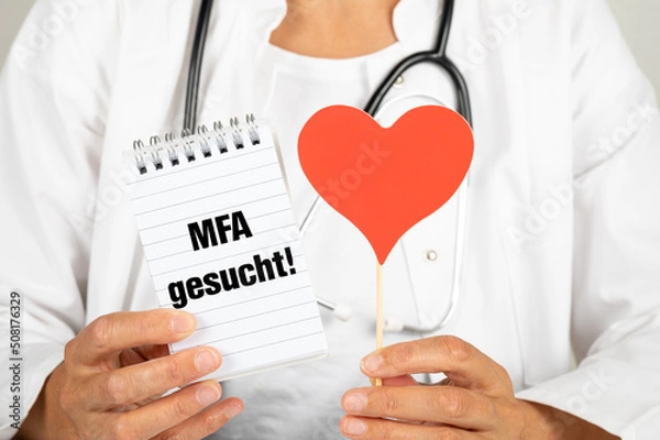 Fototapeta Hausärztin mit einem Notizblock auf dem MFA gesucht steht und einem roten Herz