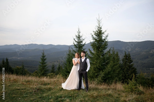 Fototapeta happy stylish bride and groom running and having fun in mountains on summer sunny day
