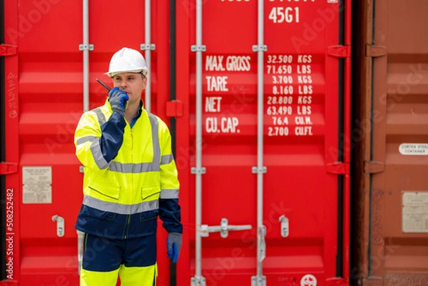 Obraz Man worker using walkie talkie to communication with colleague at container yard.