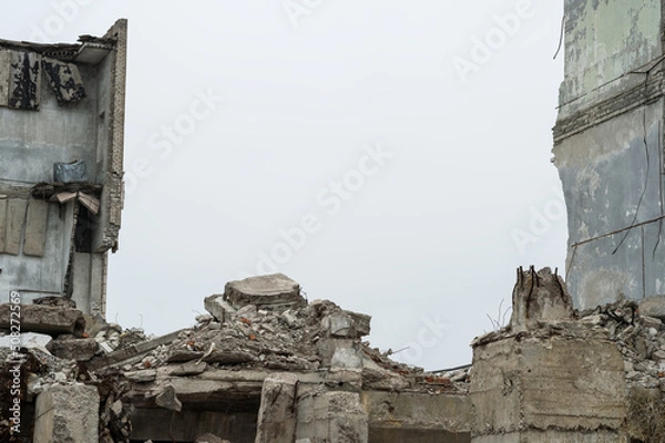 Fototapeta Gray debris of the building in the form of large concrete piles, slabs, beams with remnants of a brick wall against a gray sky. Background