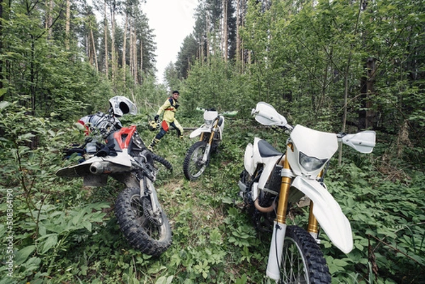 Obraz Enduro motorcyclists in deep forest at halt, checking the technical condition of motorcycles, removing logs from the path