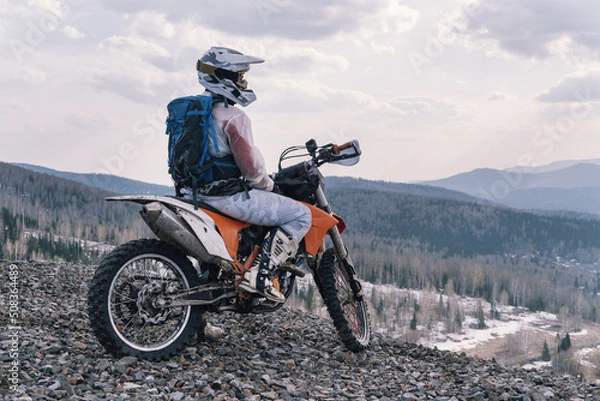 Fototapeta motorcyclist sitting on dirt motorcycle on rubble at the top of off-road mountain relaxing and enjoying the view