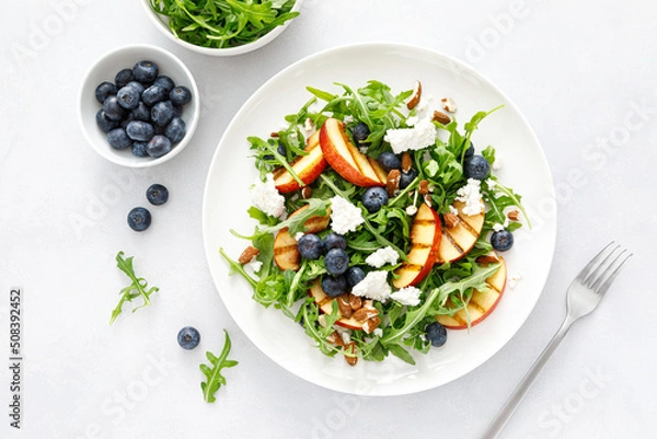 Obraz Peach, blueberry and arugula fresh fruit salad with cheese and almond nuts, top view