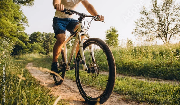 Fototapeta A man rides a bicycle on a dirt road in the summer at sunset. Active rest in the summer on bicycles.
