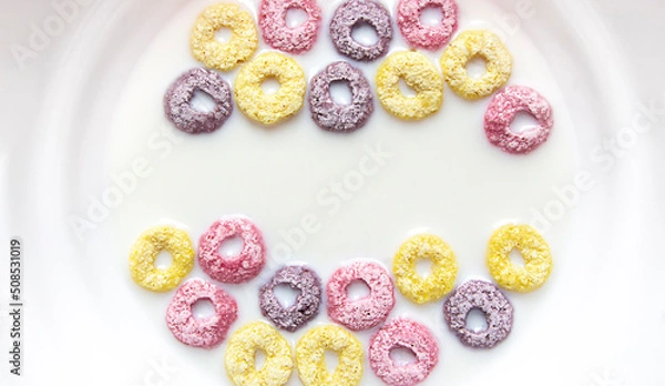 Fototapeta in a plate of milk with multi-colored rainbow rings of cereals. healthy food, fast breakfast. copy space